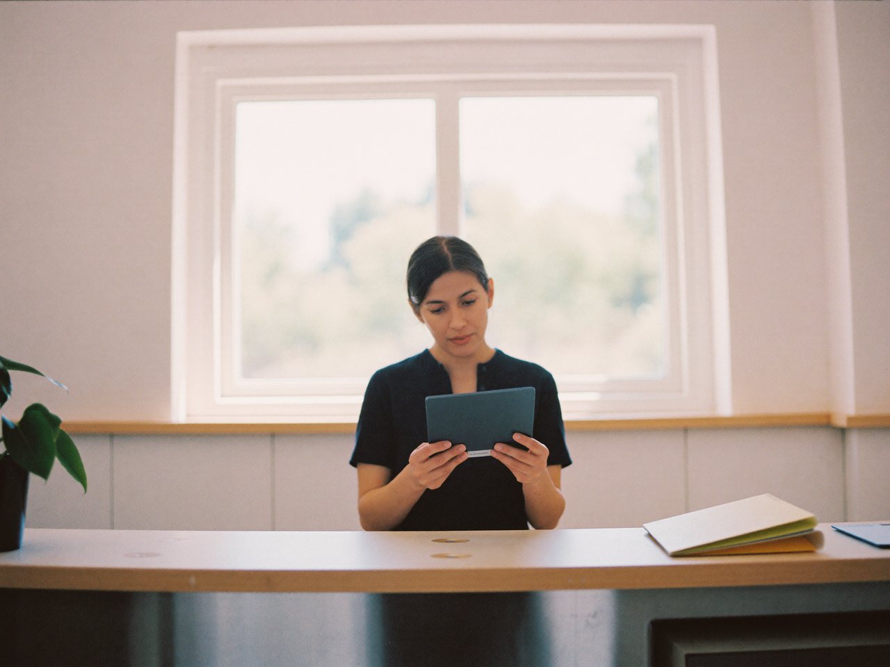 Mujer consultando una tablet en el mostrador ordenado de un pequeño negocio, con luz natural de ventana